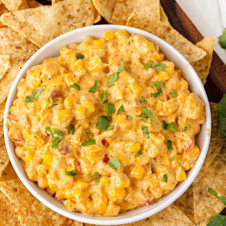 A bowl of cheesy corn dip on a platter with tortilla chips.