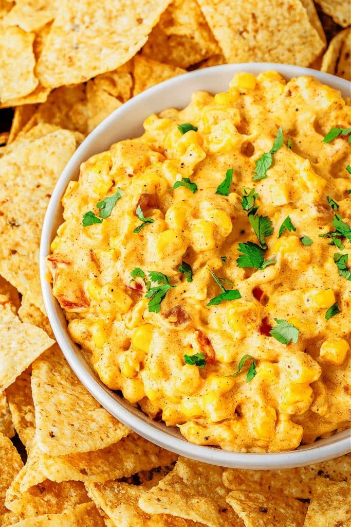 A bowl of cheesy corn dip on a platter with tortilla chips.