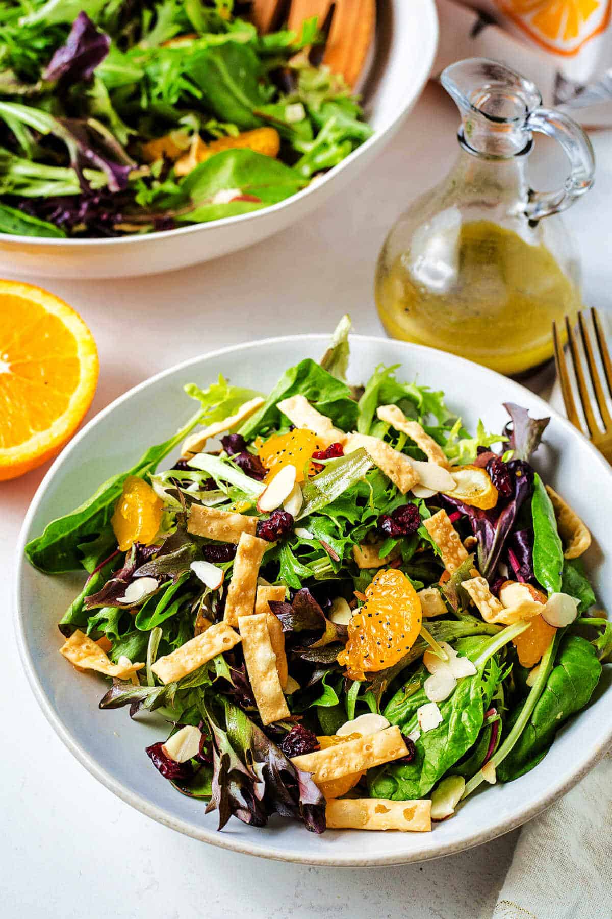 Mandarin orange salad in a serving bowl on a table with a carafe of vinaigrette to the side.