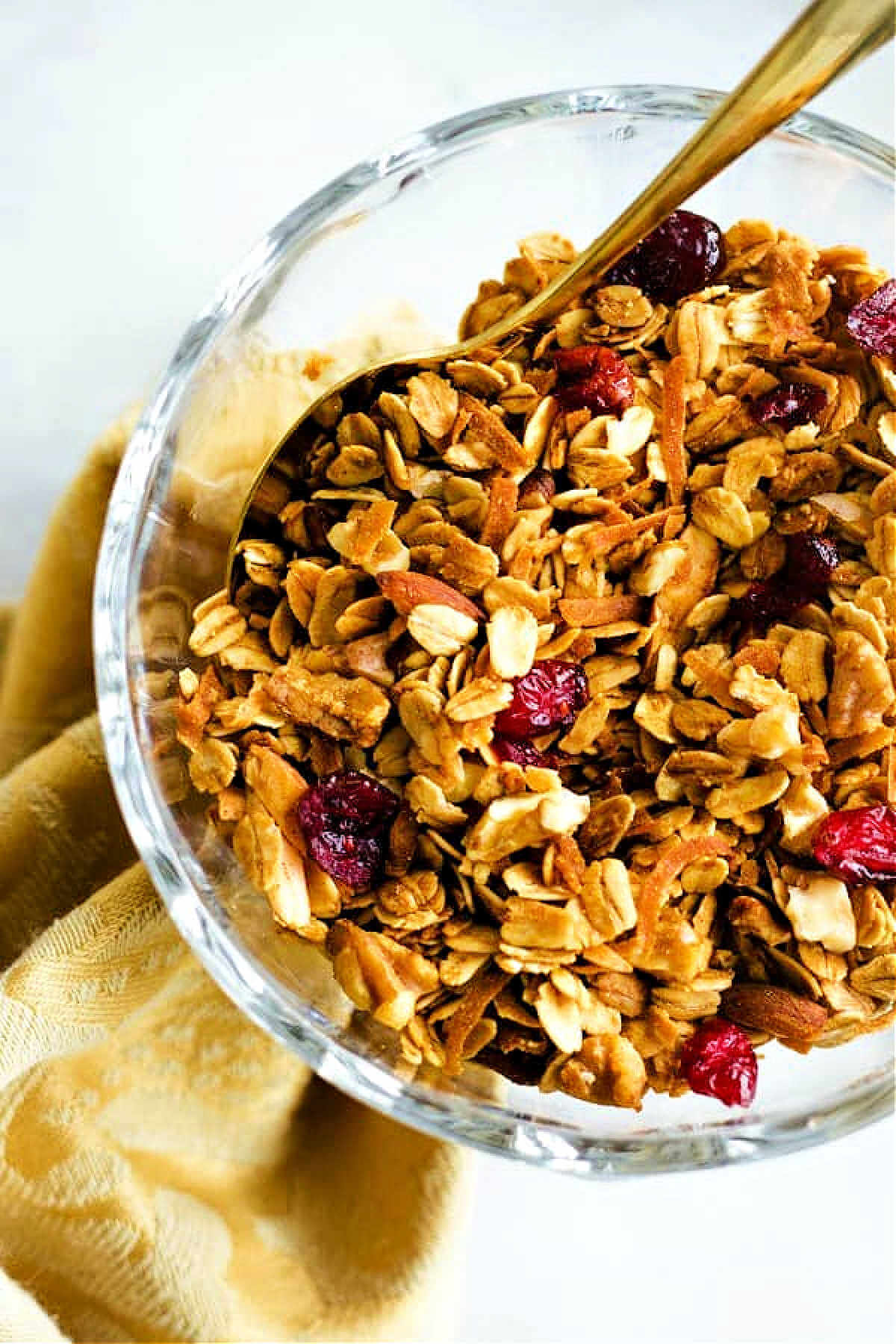A bowl of granola with nuts, toasted coconut, and dried cranberries on a table.