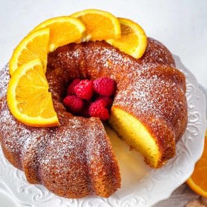 A bundt cake with a missing slice with orange slices arranged on top on a cake plate.