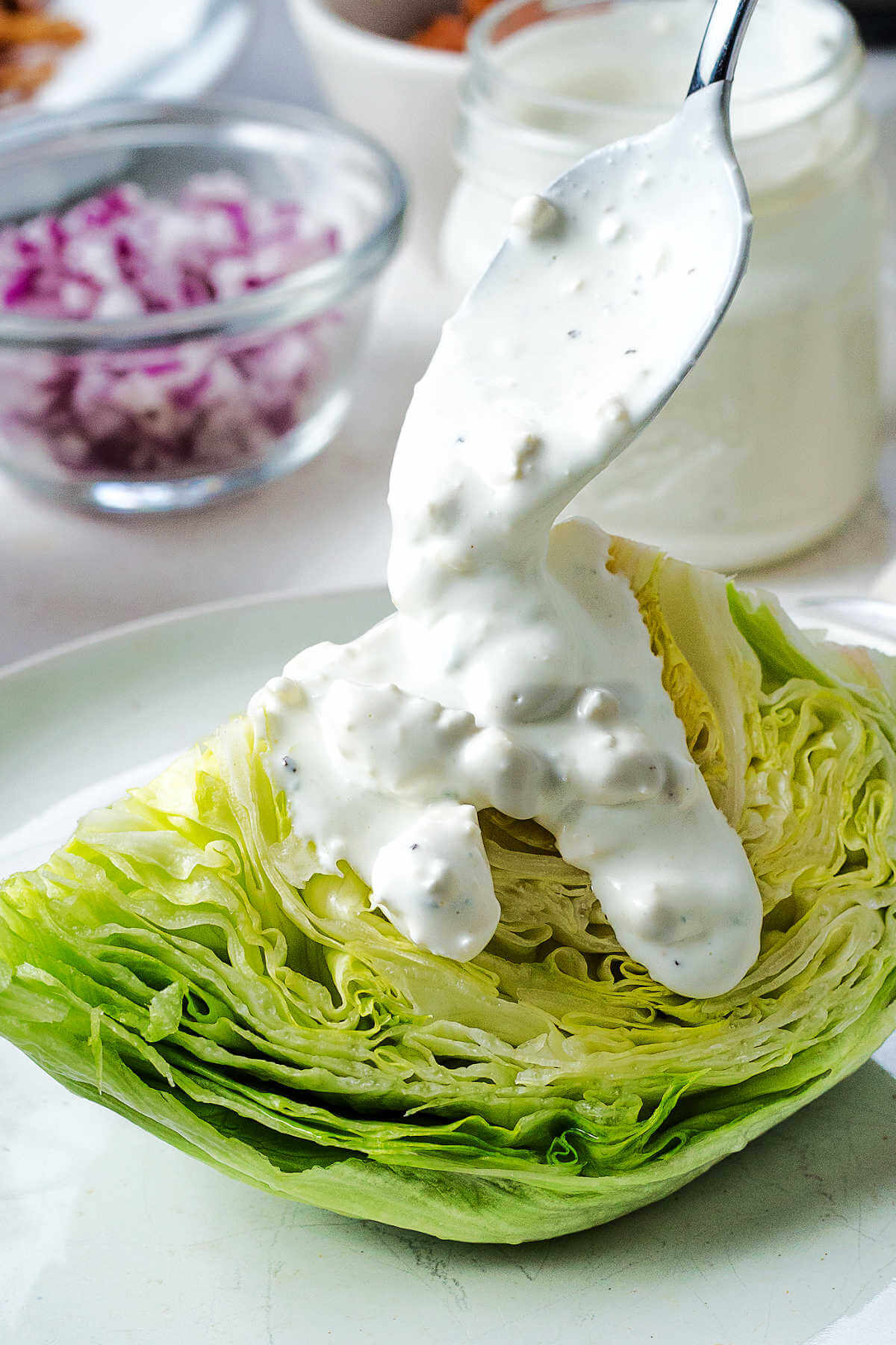 Spooning blue cheese dressing over a wedge of lettuce on a plate.