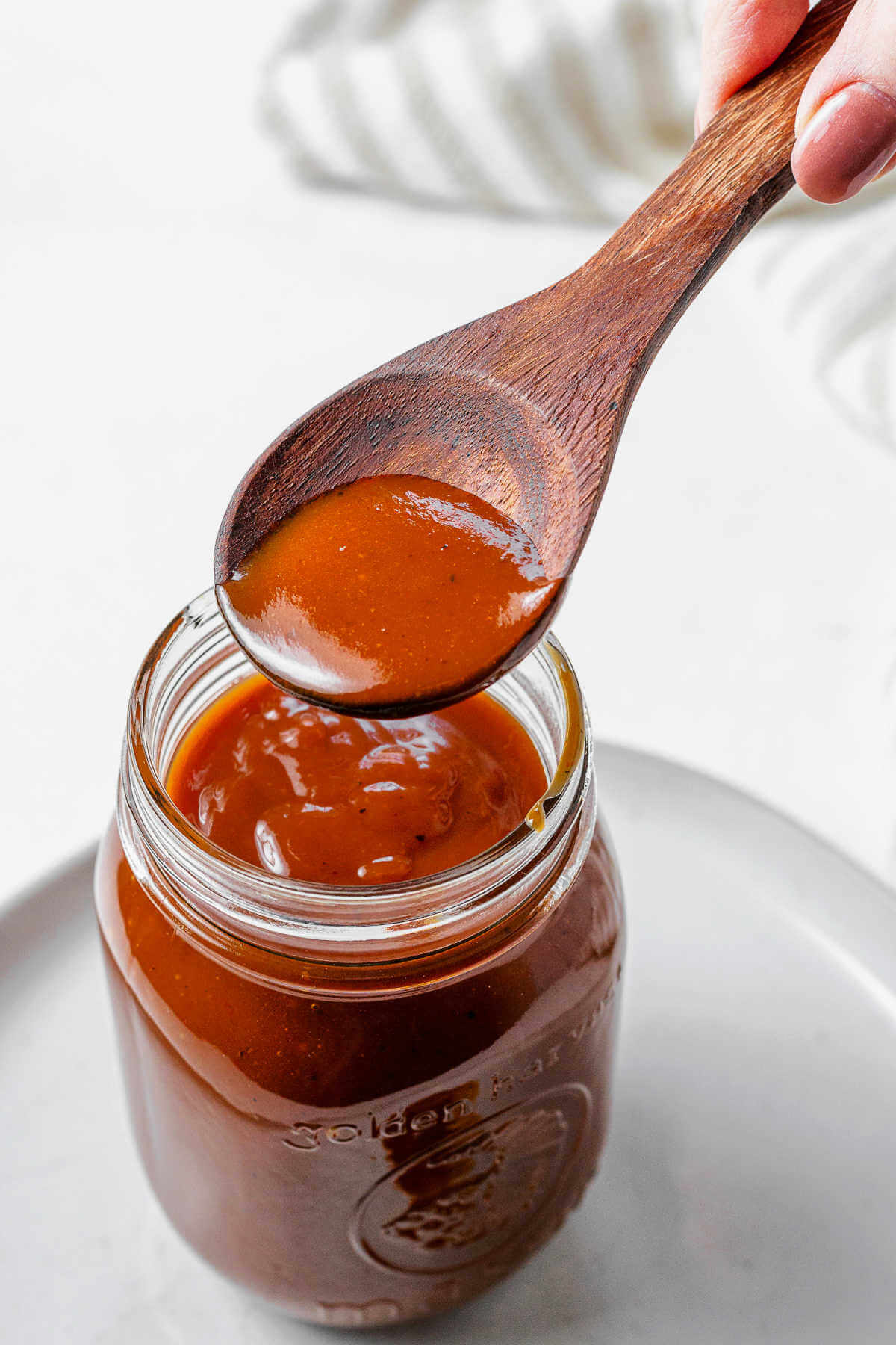 Spooning sauce into a mason jar sitting on a plate.