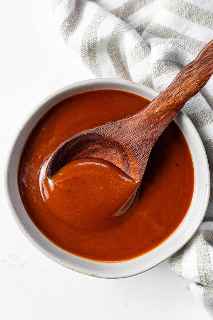 A bowl of homemade BBQ sauce with a wooden spoon on a table.