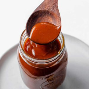 Spooning sauce into a mason jar sitting on a plate.