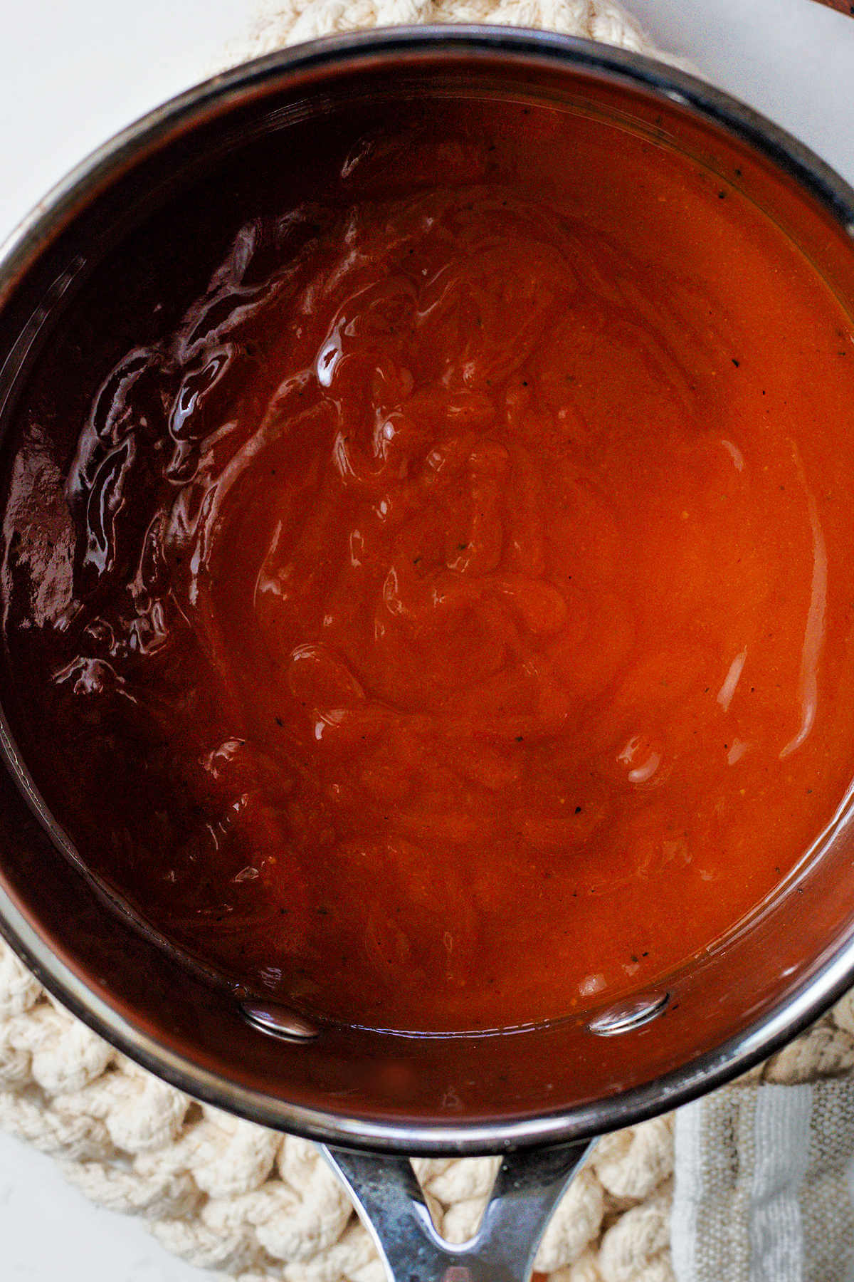 Barbecue sauce in a saucepan on a hot pad.