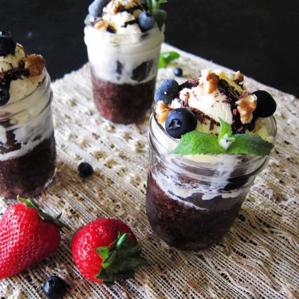 Brownie Sundaes in mason jars on a table with strawberries.
