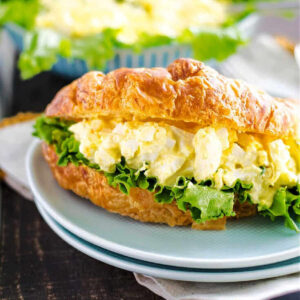 Egg Salad on a croissant on a plate on a table.