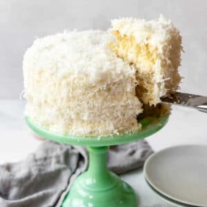Coconut Cake on a pedestal with a slice being lifted out.