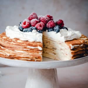 A Crepe Cake on a cake stand with a slice missing.