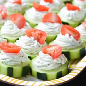 Cucumber slices with dill dip and tomatoes on a plate.