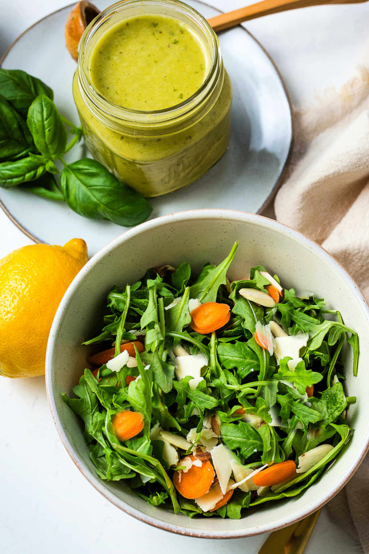 An arugula salad in a bowl and a jar of salad dressing on a table.