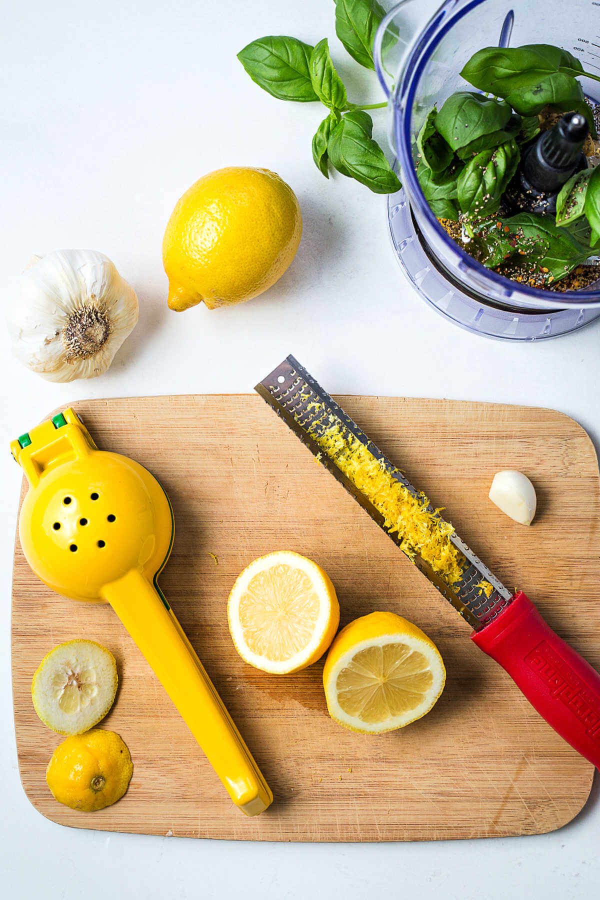 A halved lemon, a zester, and a citrus press on a cutting board on a table.