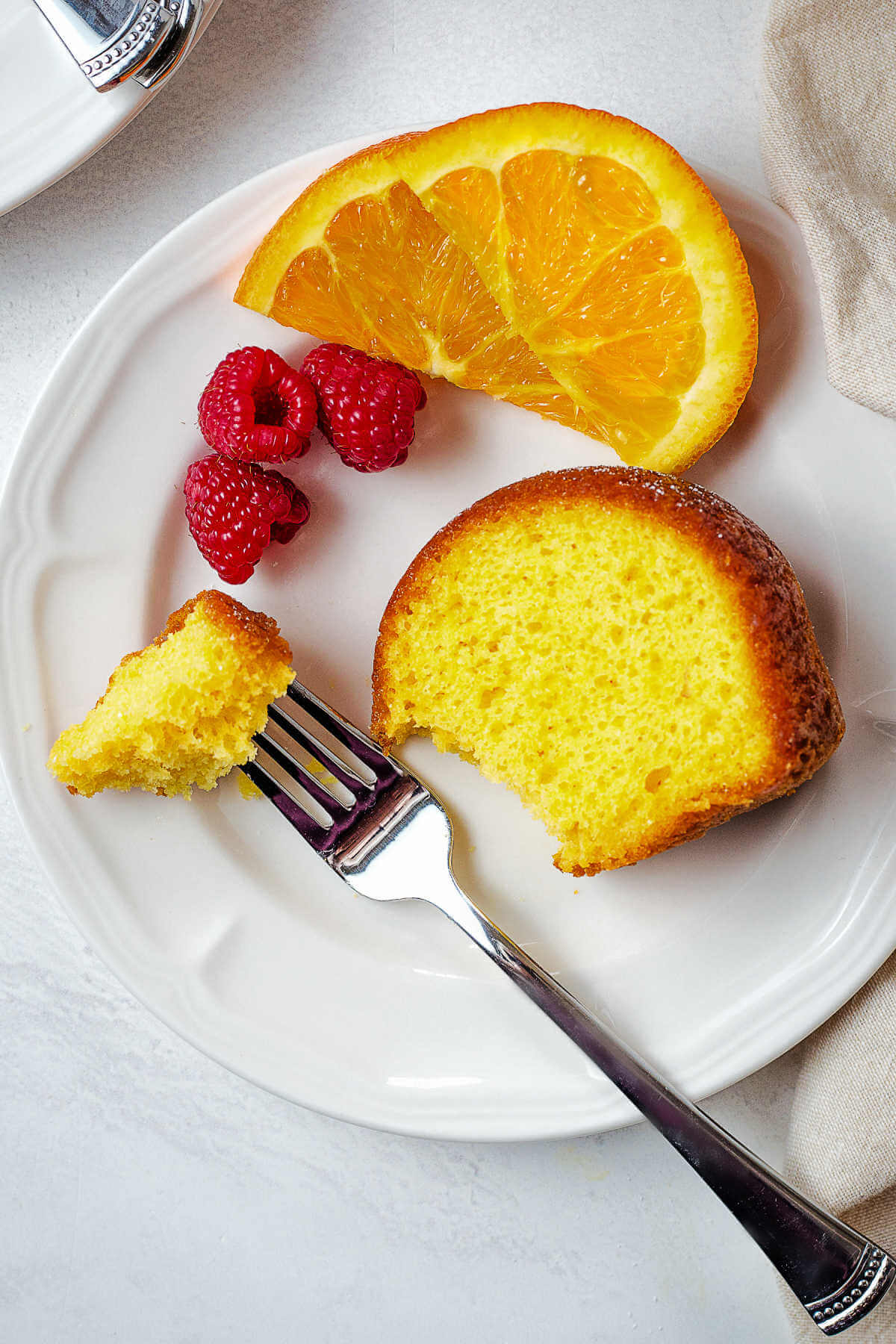 A slice of orange cake on a plate with a fork on a table.