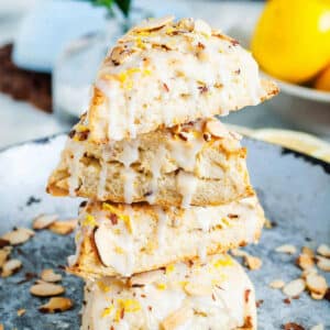 Glazed lemon scones with almonds stacked on a plate on a table.