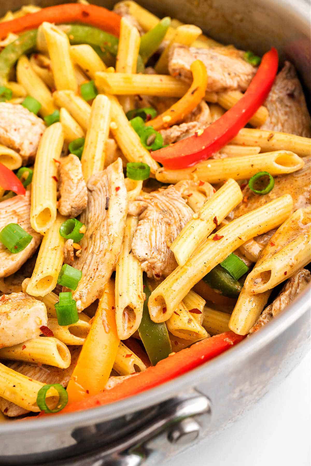 Penne pasta with bell peppers and chicken in a jerk sauce in a skillet.