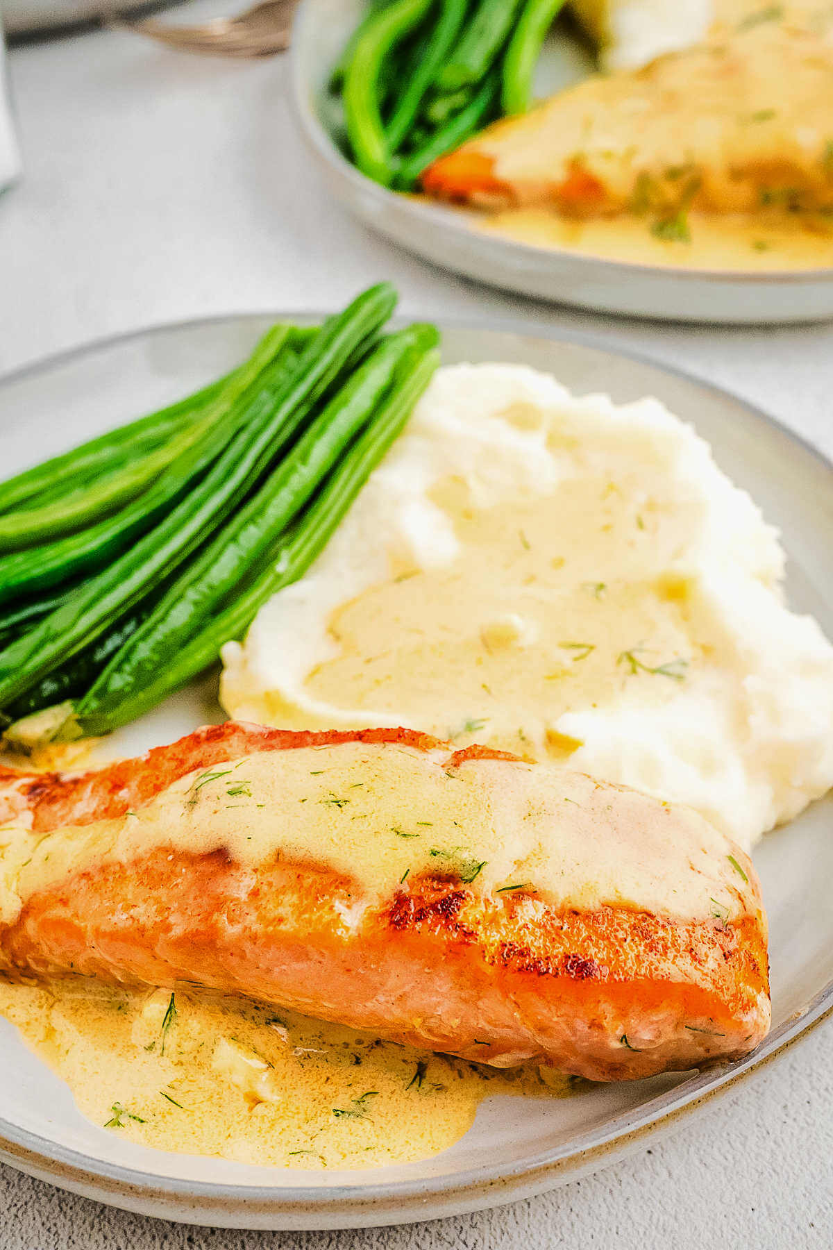 Close up and side view of a salmon filet topped with cream sauce on a plate.