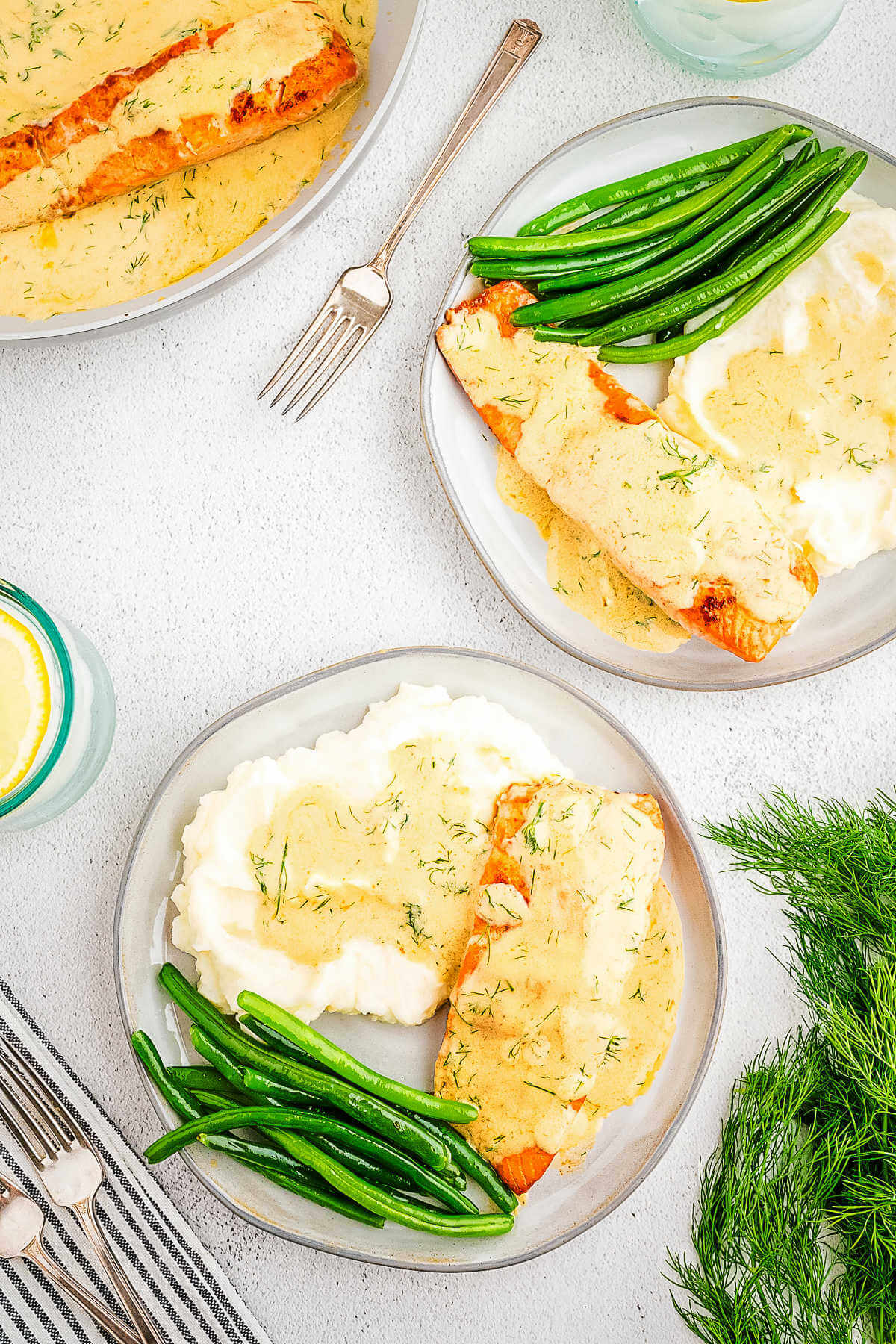 A dinner table set with plates of salmon, mashed potatoes, and green beans.
