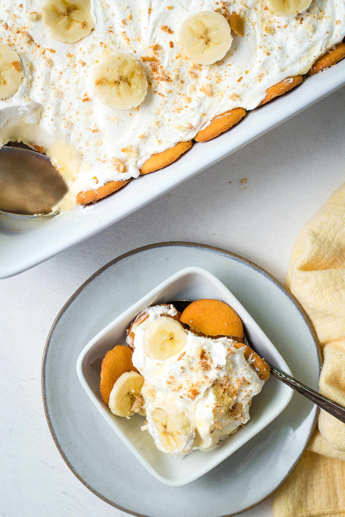 A serving of banana pudding in a bowl with a full pudding in the background on a table.