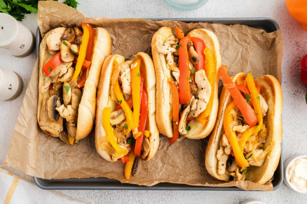 Chicken Philly Sandwiches with bell peppers, onions, and mushrooms on a piece of parchment paper on a baking tray.