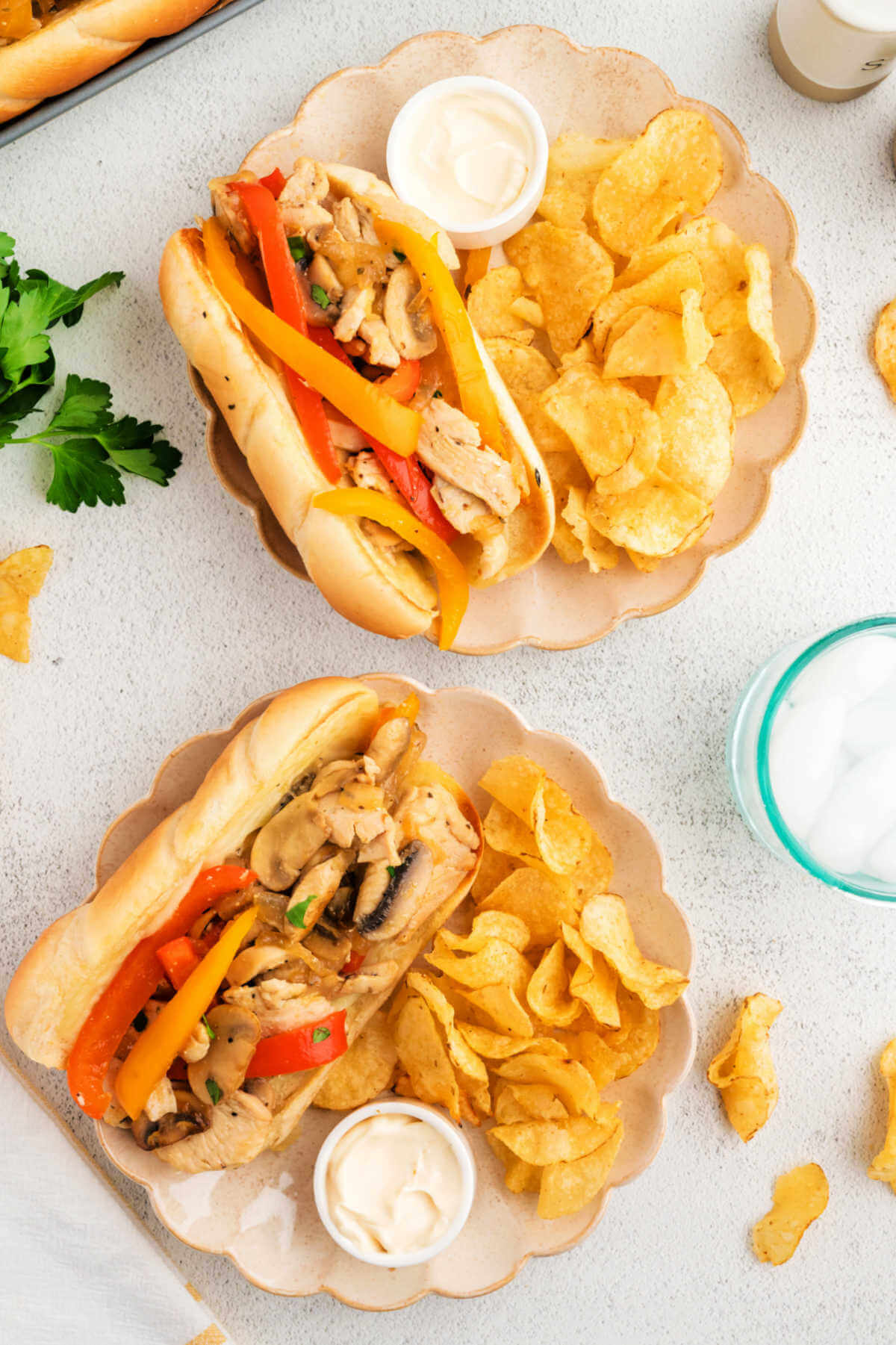 Chicken Philly Sandwiches on a plate with potato chips on a table.