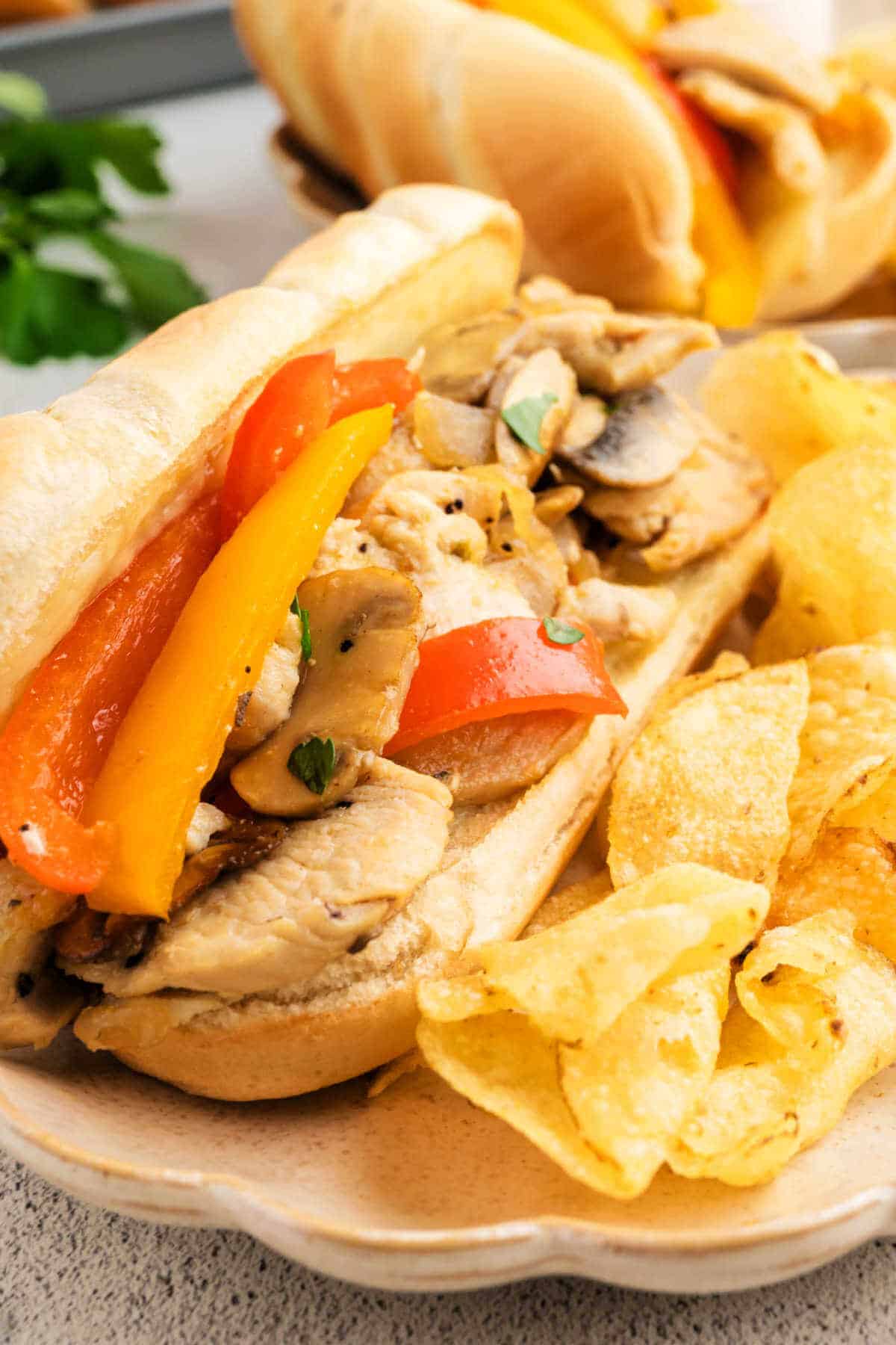 Close up view of a Chicken Philly on a plate with potato chips on a table.