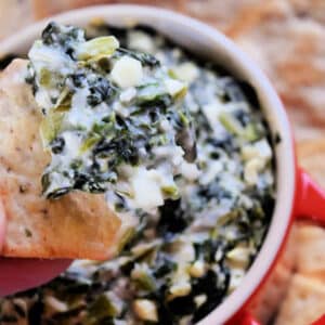 Spanakopita Dip in a bowl with a cracker being dipped into it.