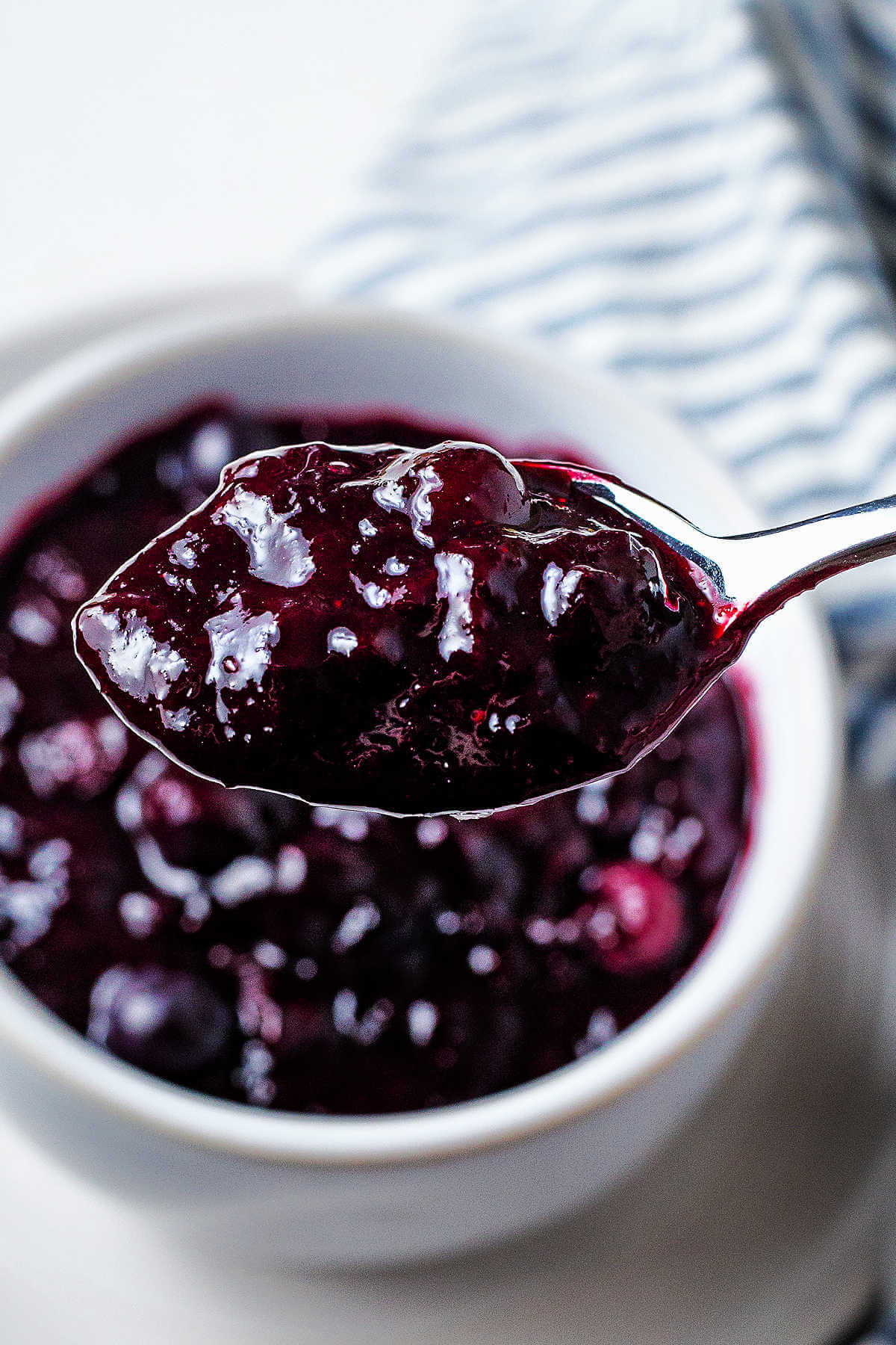 A spooful of blueberry compote being lifted out of a bowl.