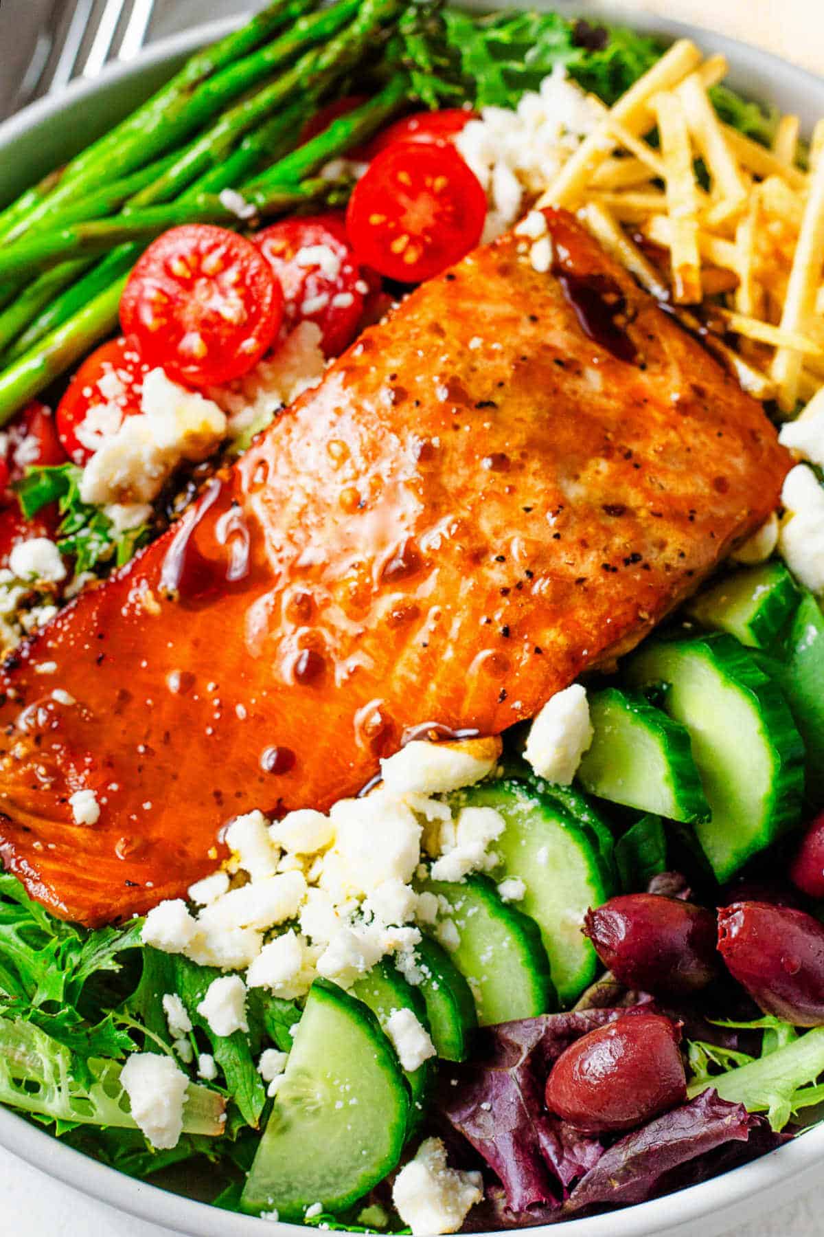 A grilled salmon filet drizzled with balsamic dressing on a bowl of salad on a table.