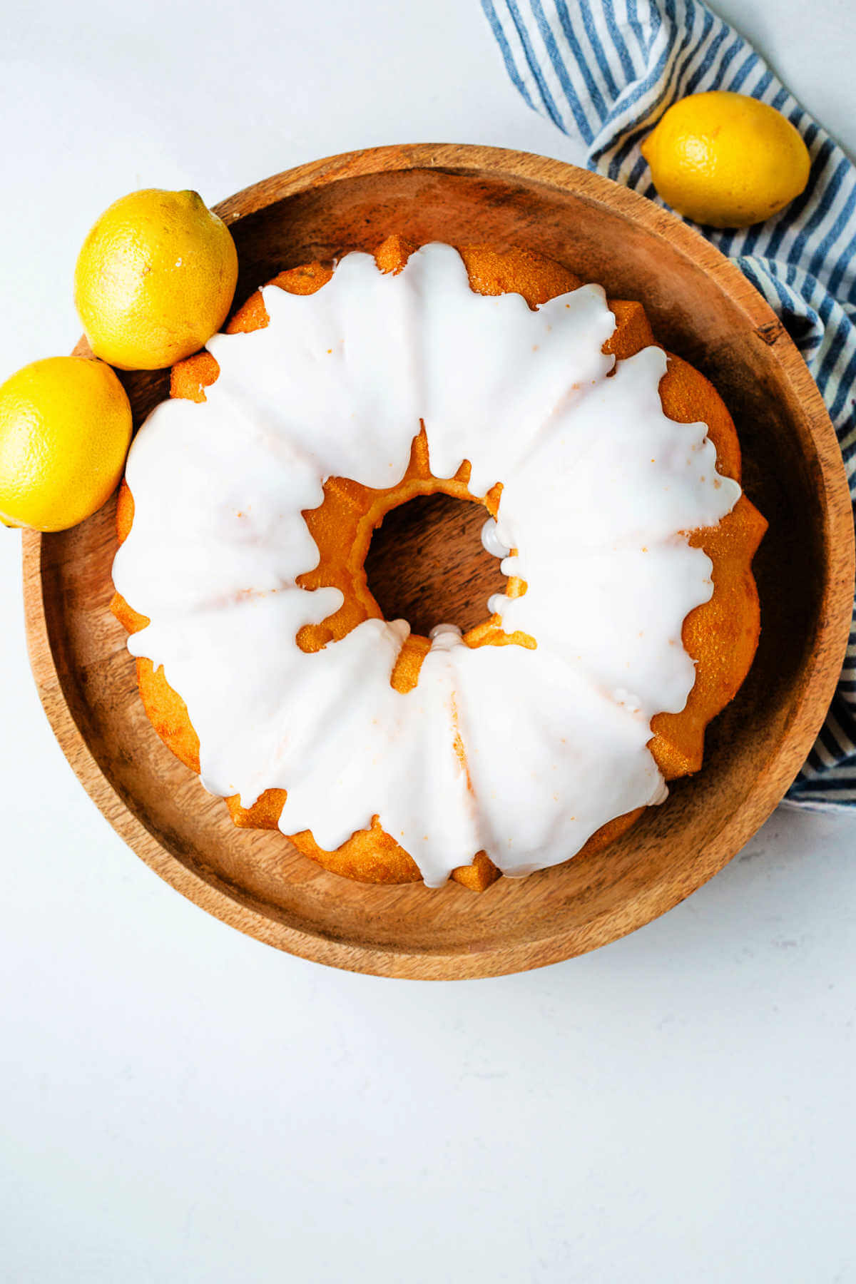 Lemon Bundt Cake with a powdered sugar glaze on a wooden cake stand with lemons on the side.