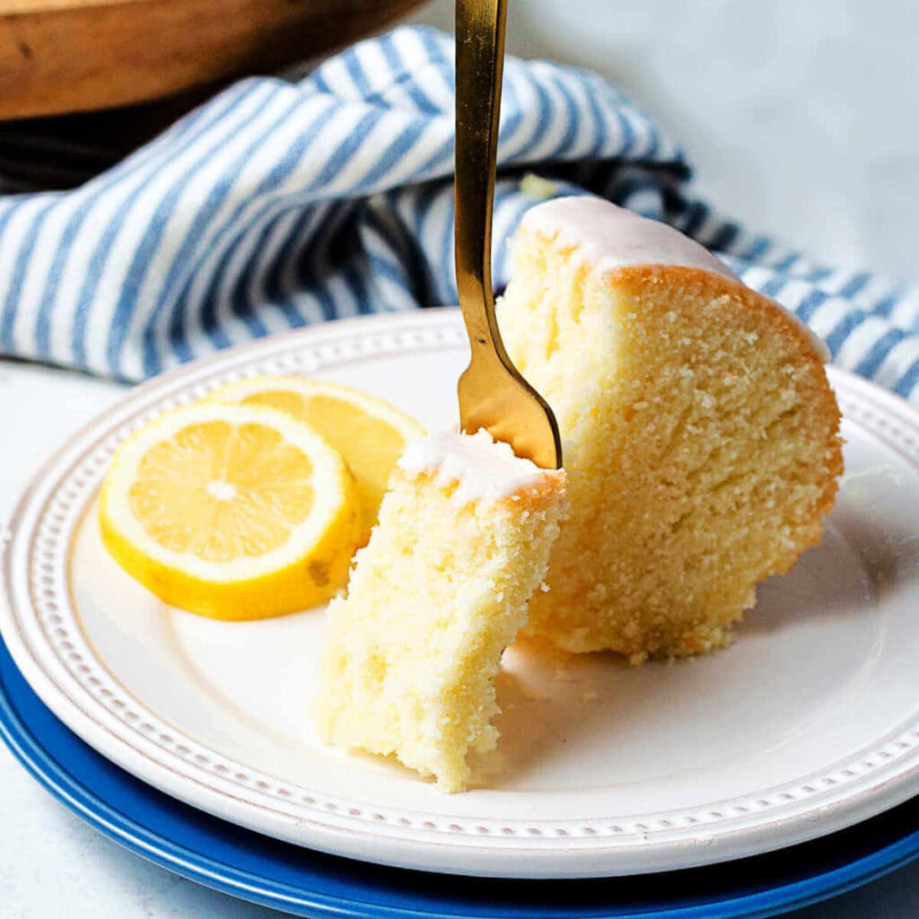 A fork cutting through a piece of pound cake on a plate.