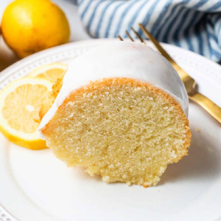 A slice of Lemon Bundt Cake on a plate with lemon slices and a gold fork.