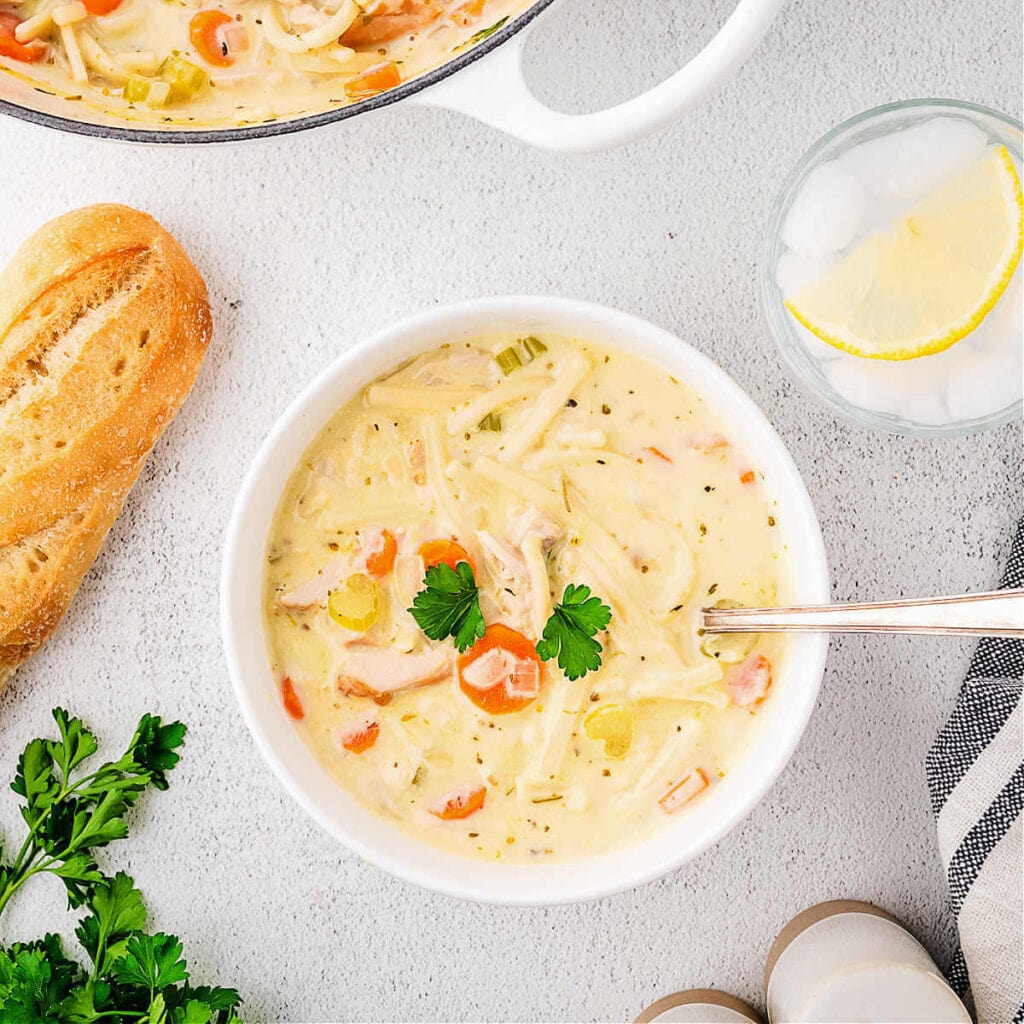 A bowl of creamy turkey noodle soup on a table with a loaf of brad.