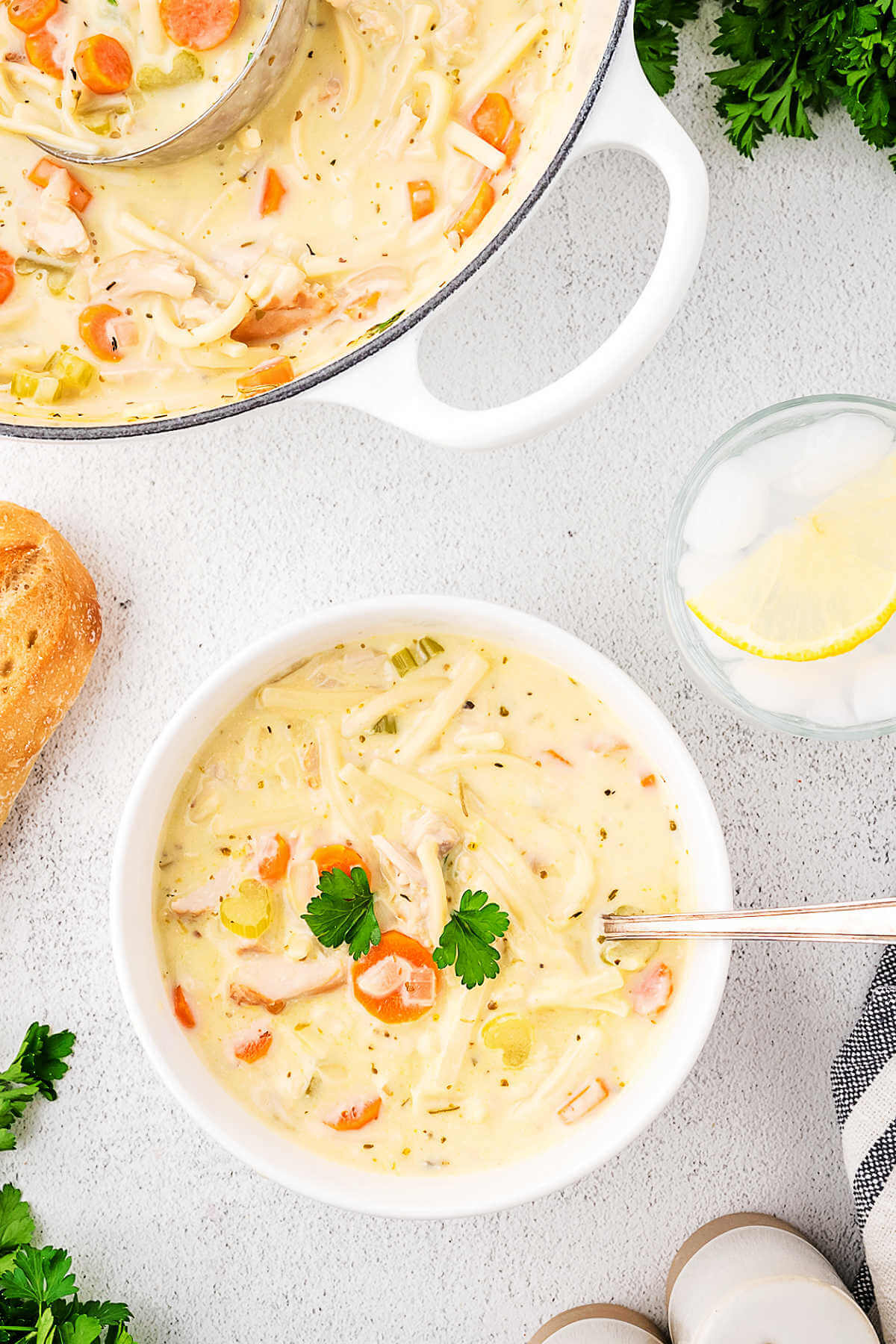 A bowl of turkey noodle soup on a table with move soup in a pot in the background.