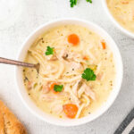 A bowl of creamy turkey noodle soup on a table with a loaf of brad.