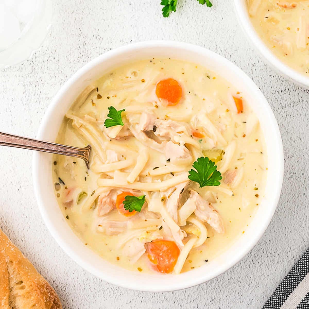 A bowl of creamy turkey noodle soup on a table with a loaf of brad.