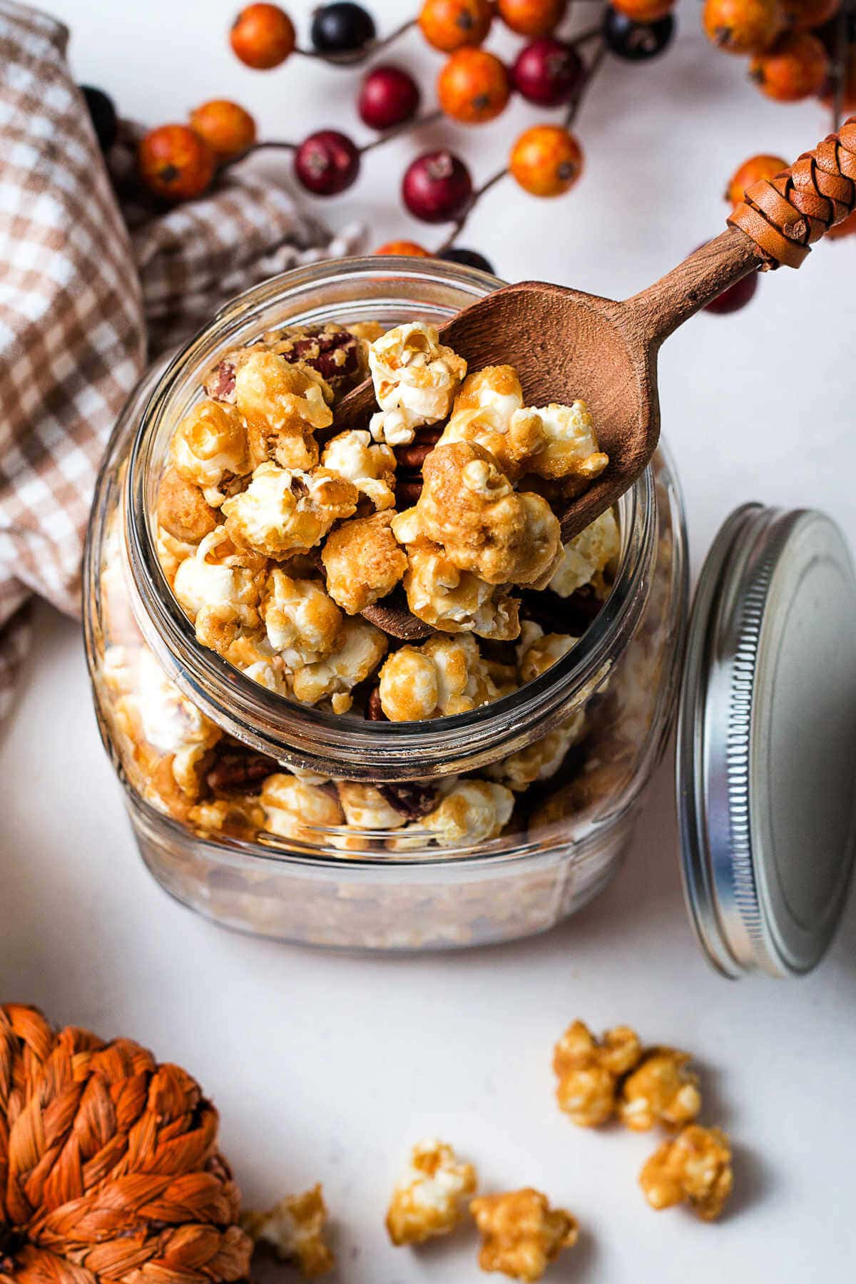 Homemade caramel corn in a glass jar with a wooden scoop on a table.