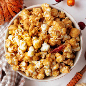 Homemade caramel corn with pecans and cashews in a bowl on a table with fall decor.