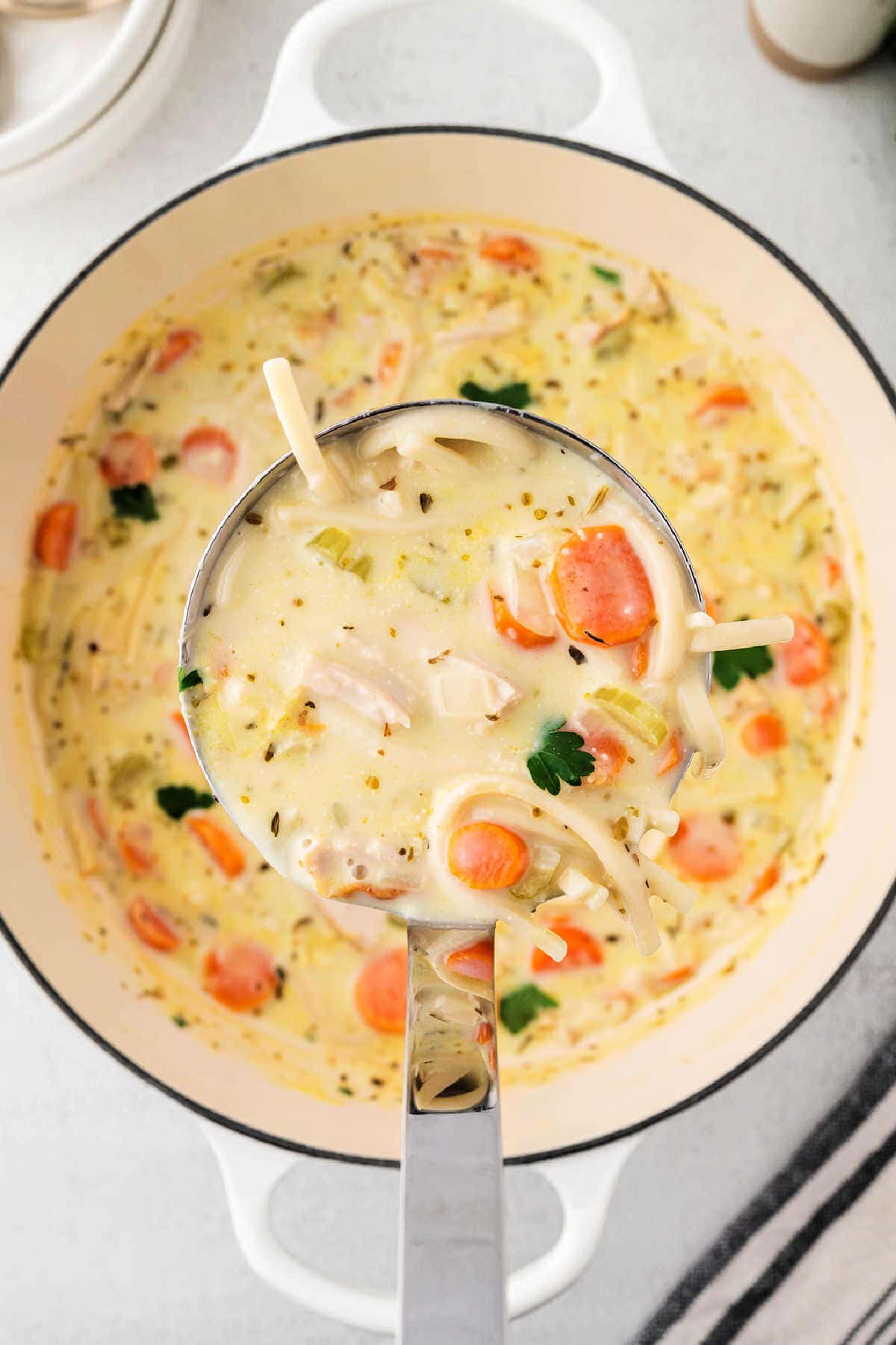 A ladle of turkey noodle soup being lifted out of a pot of soup.