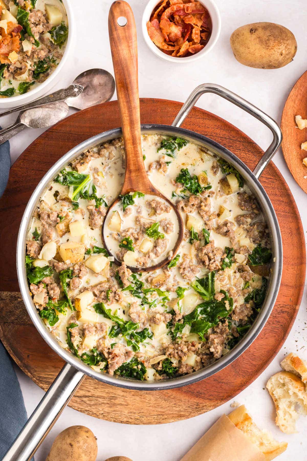 A Dutch oven with zuppa toscana soup on a table with crusty bread.