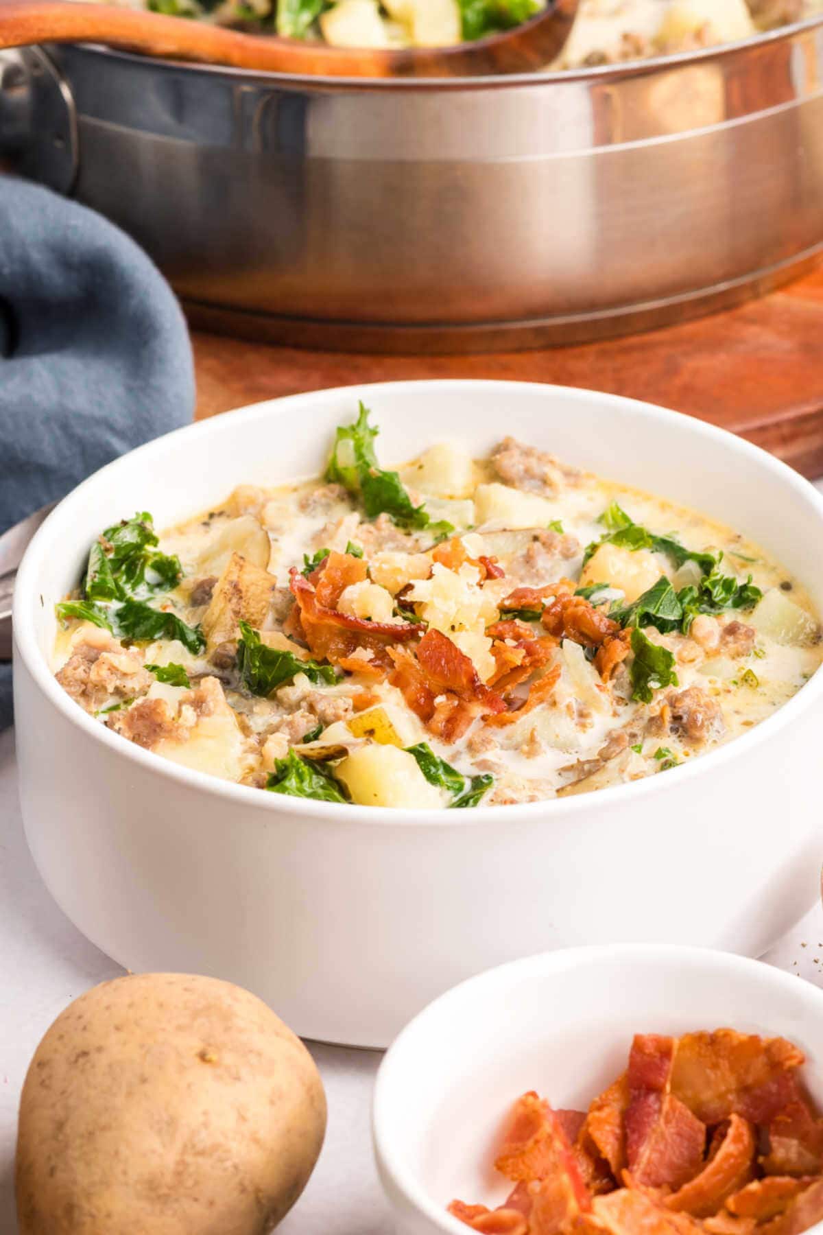 A bowl of soup with crispy bacon and a pot of soup on a table.