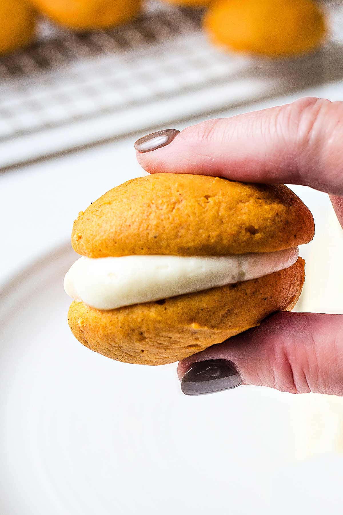 Holding a pumpkin whoopie pie between thumb and finger showing cream cheese filling.