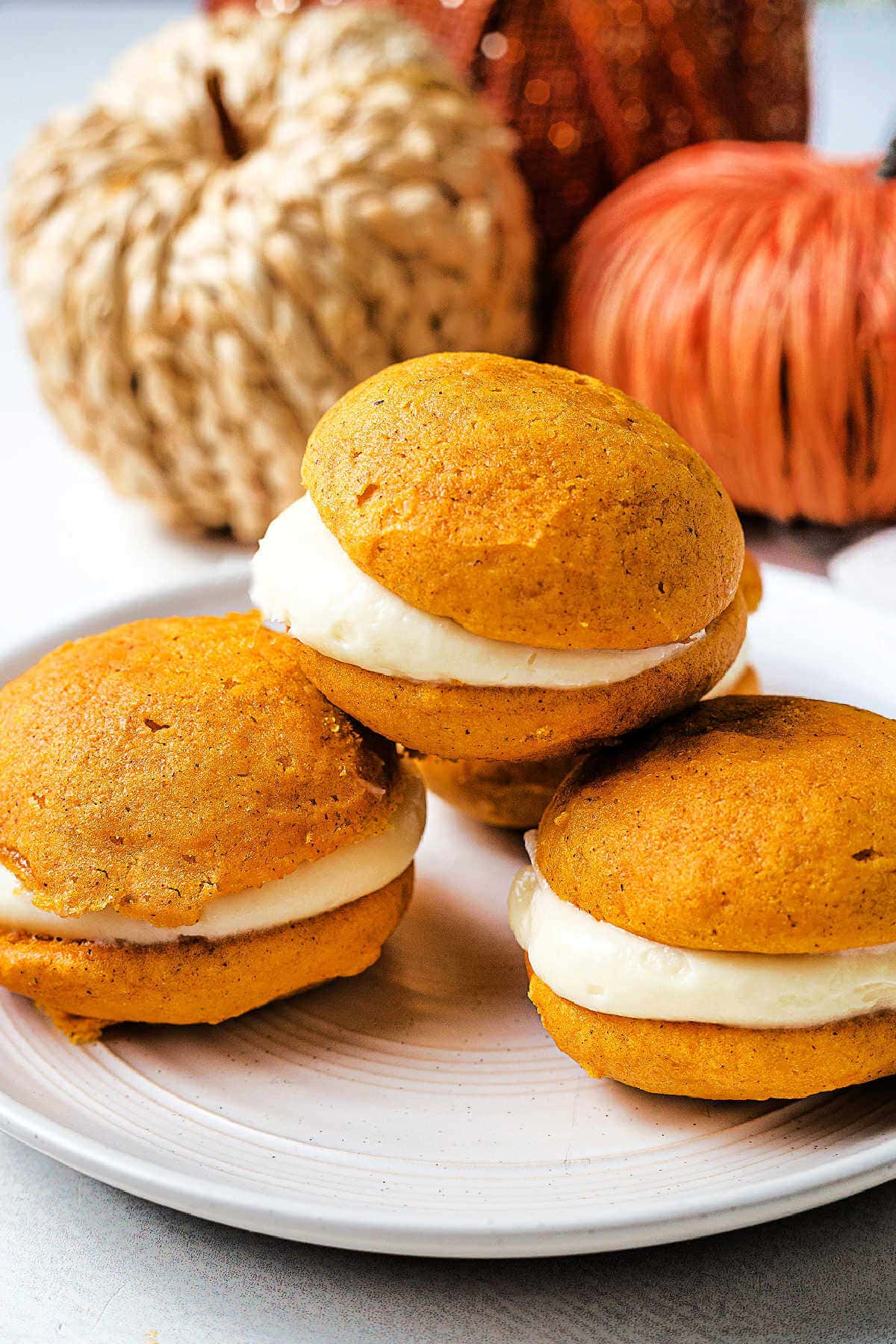 Pumpkin whoopie pies on a plate on a table with Fall decor in the background.