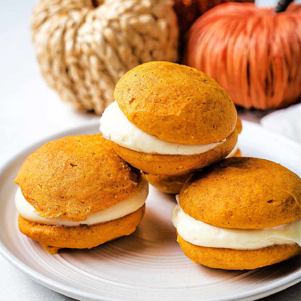 Pumpkin whoopie pies on a plate on a table with Fall decor in the background.