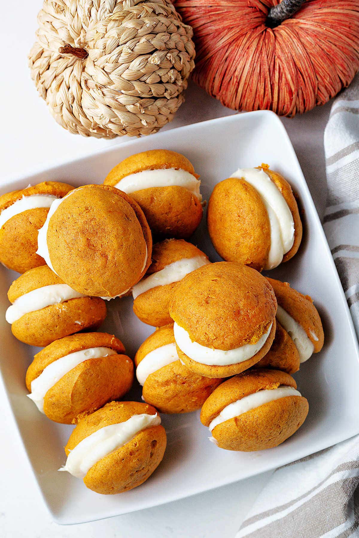 Pumpkin whoopie pies piled into a serving bowl on a table with pumpkin decor in the background.