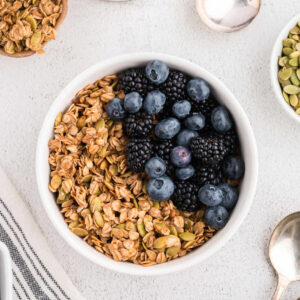 Cinnamon Maple Granola in a bowl with fresh blueberries and blackberries on a table.