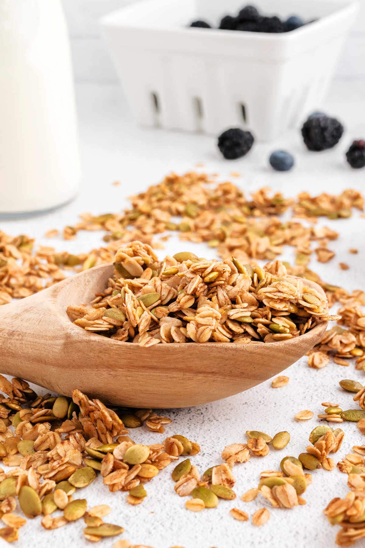 A scoop of granola on a table with berries in the background.