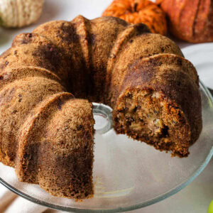 Apple bundt cake on a cake stand with a slice missing.