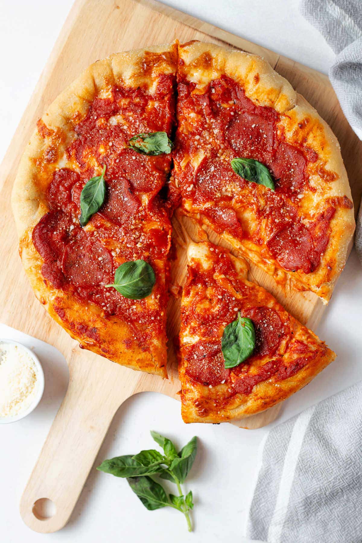 Pepperoni pizza on a pizza wheel on a table with grated parmesan cheee in a small bowl to the side.