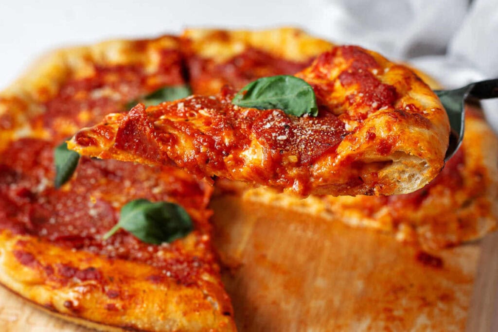 A slice of pizza being lifted up on a spatula with pizza in the background.